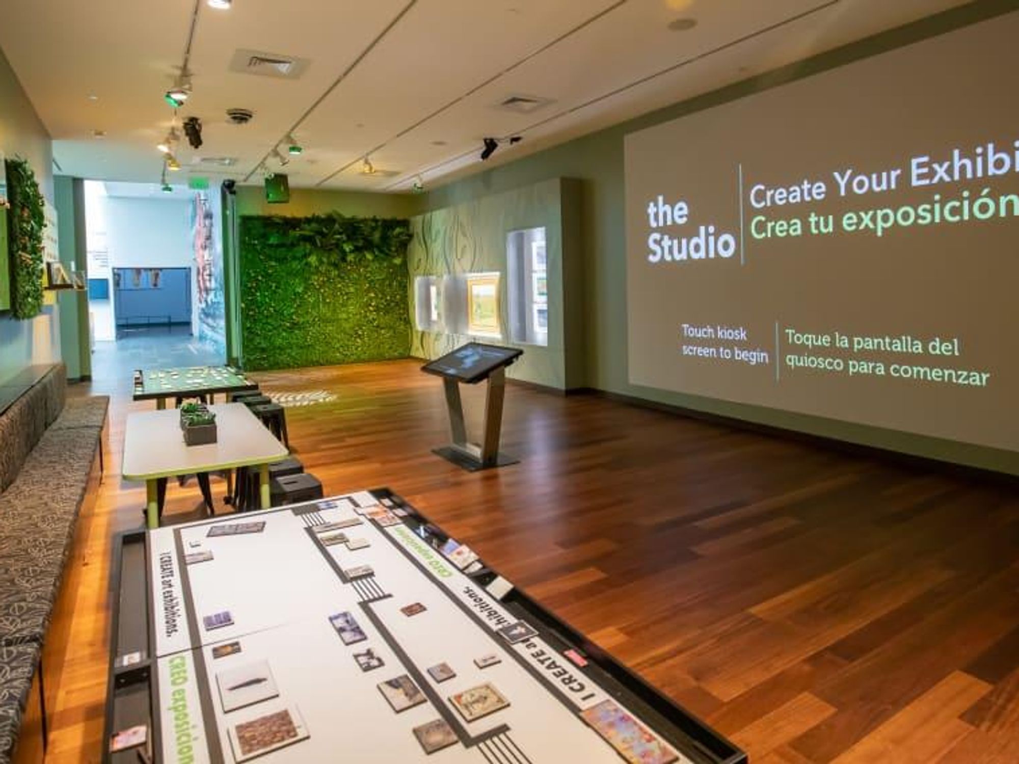 A room with multiple work stations, a projection screen, and a wall disguised as a hedge, at the McNey Art Museum's interactive studio.