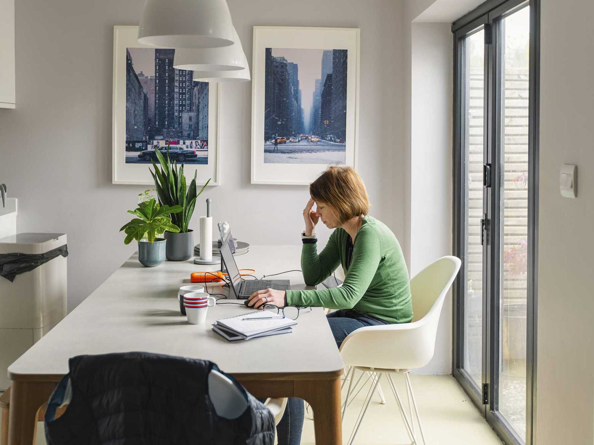 A stressed mature woman works from her dining table at home