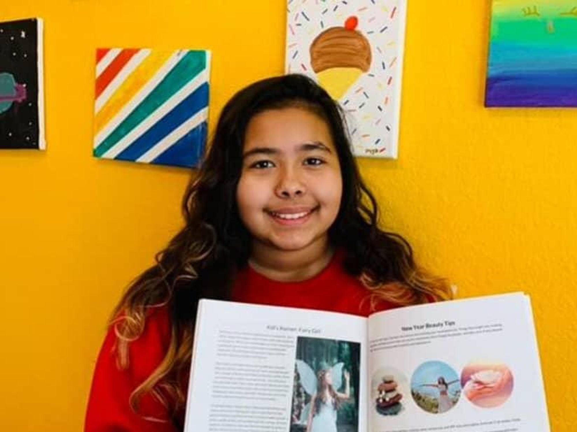 A student smiles, holding open a magazine to a story they wrote.