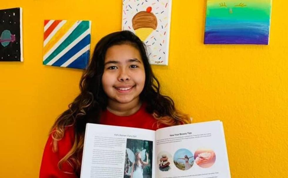 A student smiles, holding open a magazine to a story they wrote.