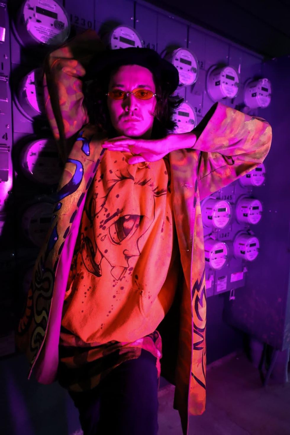 Antonio Padron, a.k.a. Akasha Luxe, poses in pink light wearing florescent patterns.