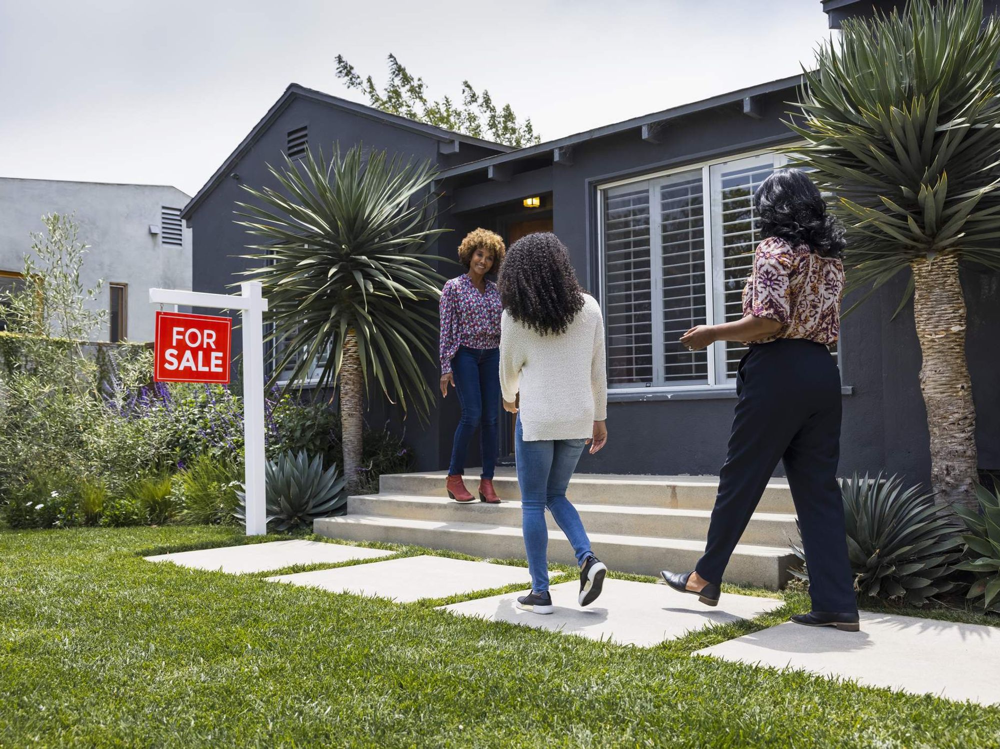 Full length of saleswoman greeting female customers while standing outside house