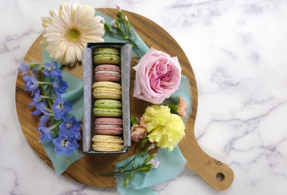 Macarons in pastel colors sit among flowers.