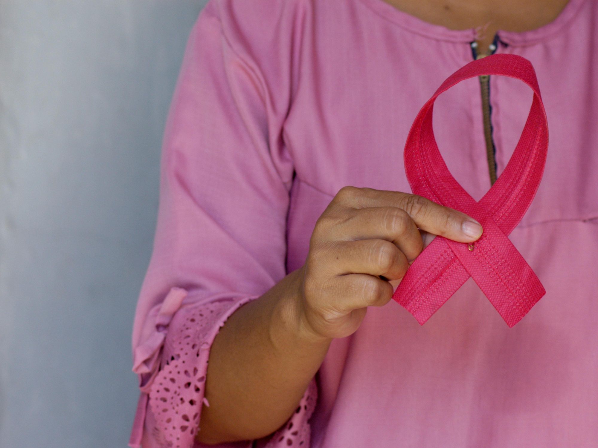 Person holding pink ribbon, San Antonio breast cancer awareness.