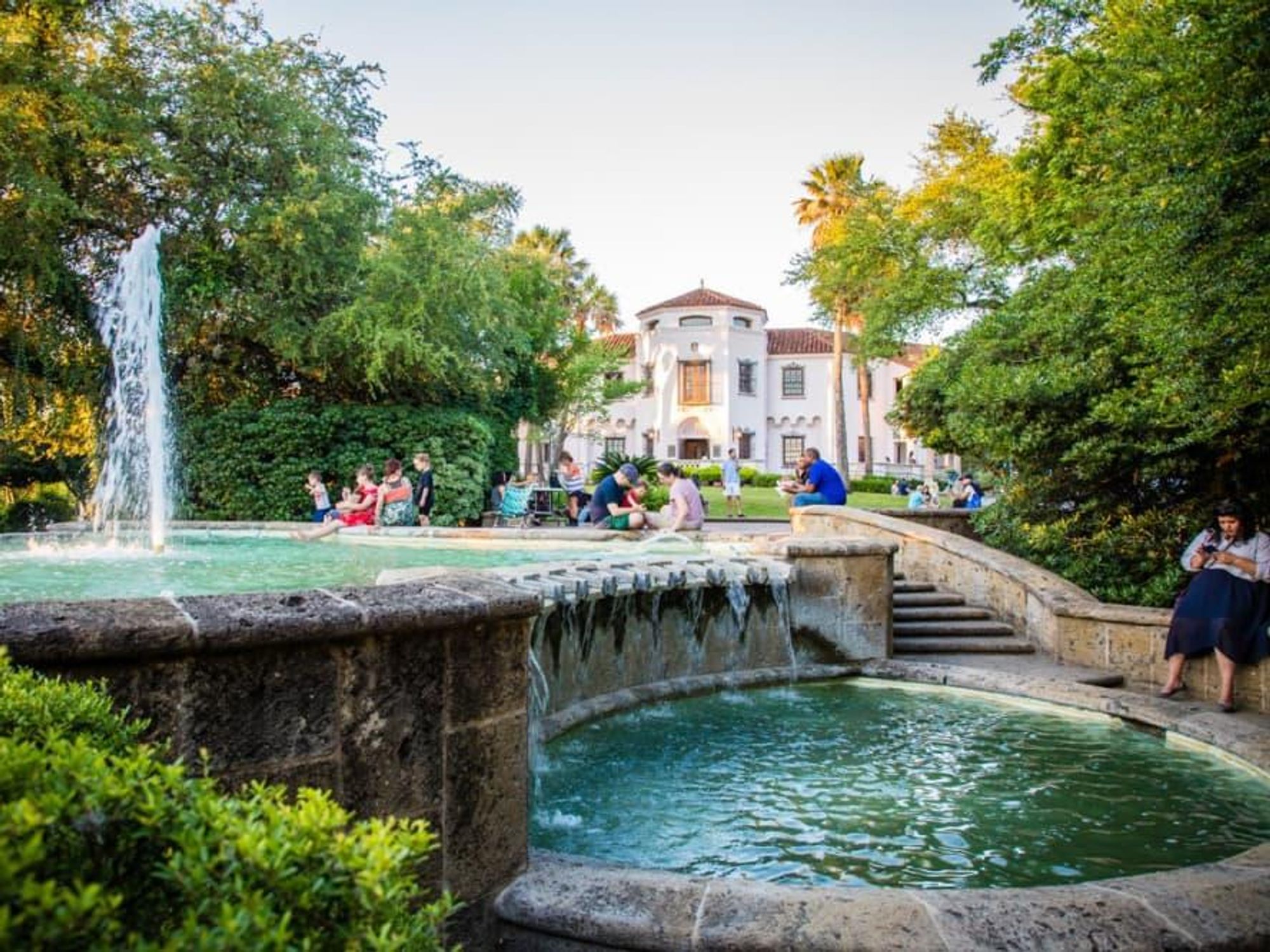 The Spanish-revival McNay mansion behind a water fountain and a crowd of visitors.
