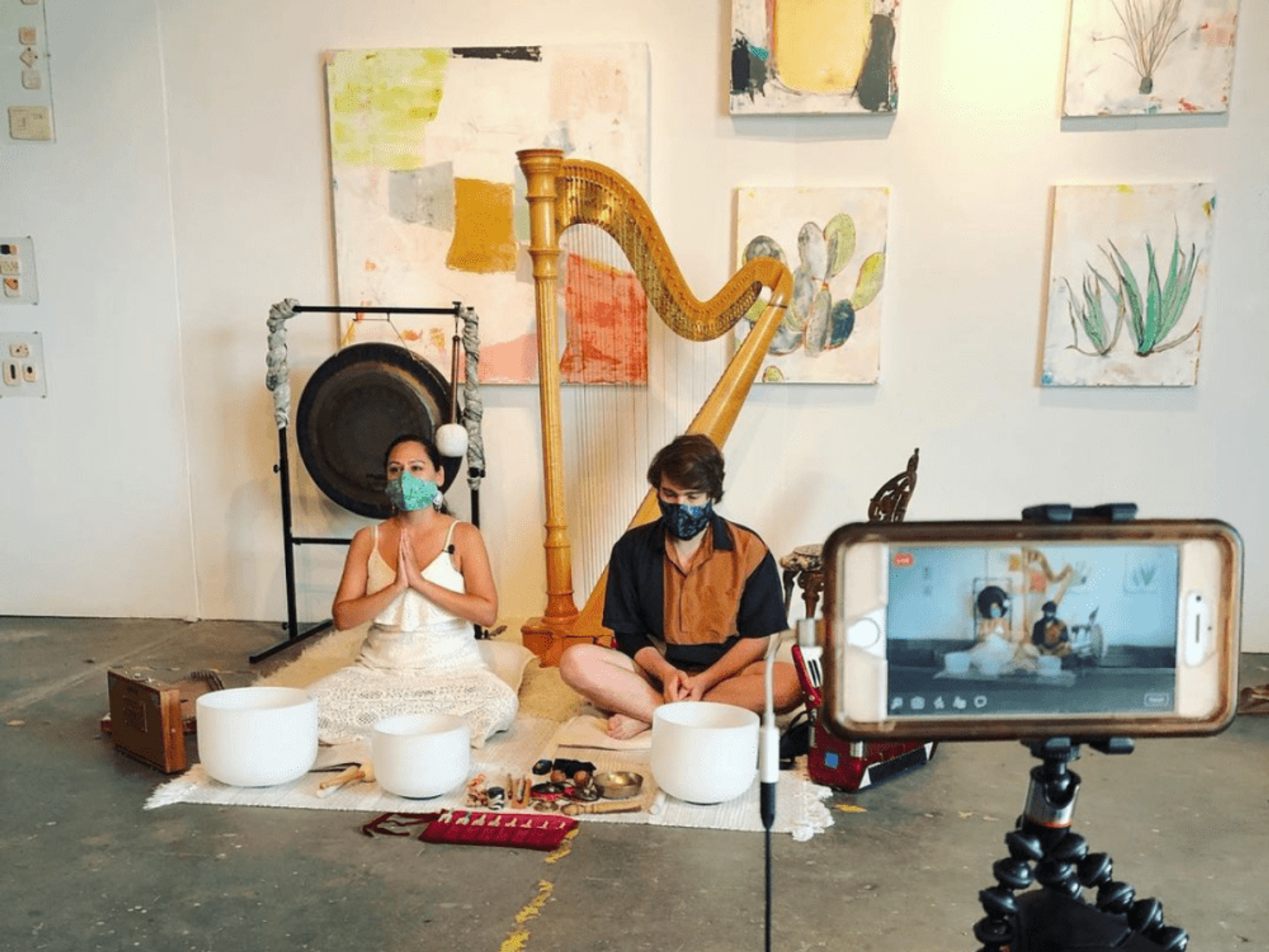 Two musicians sit among crystal singing bowls, a harp and paintings.