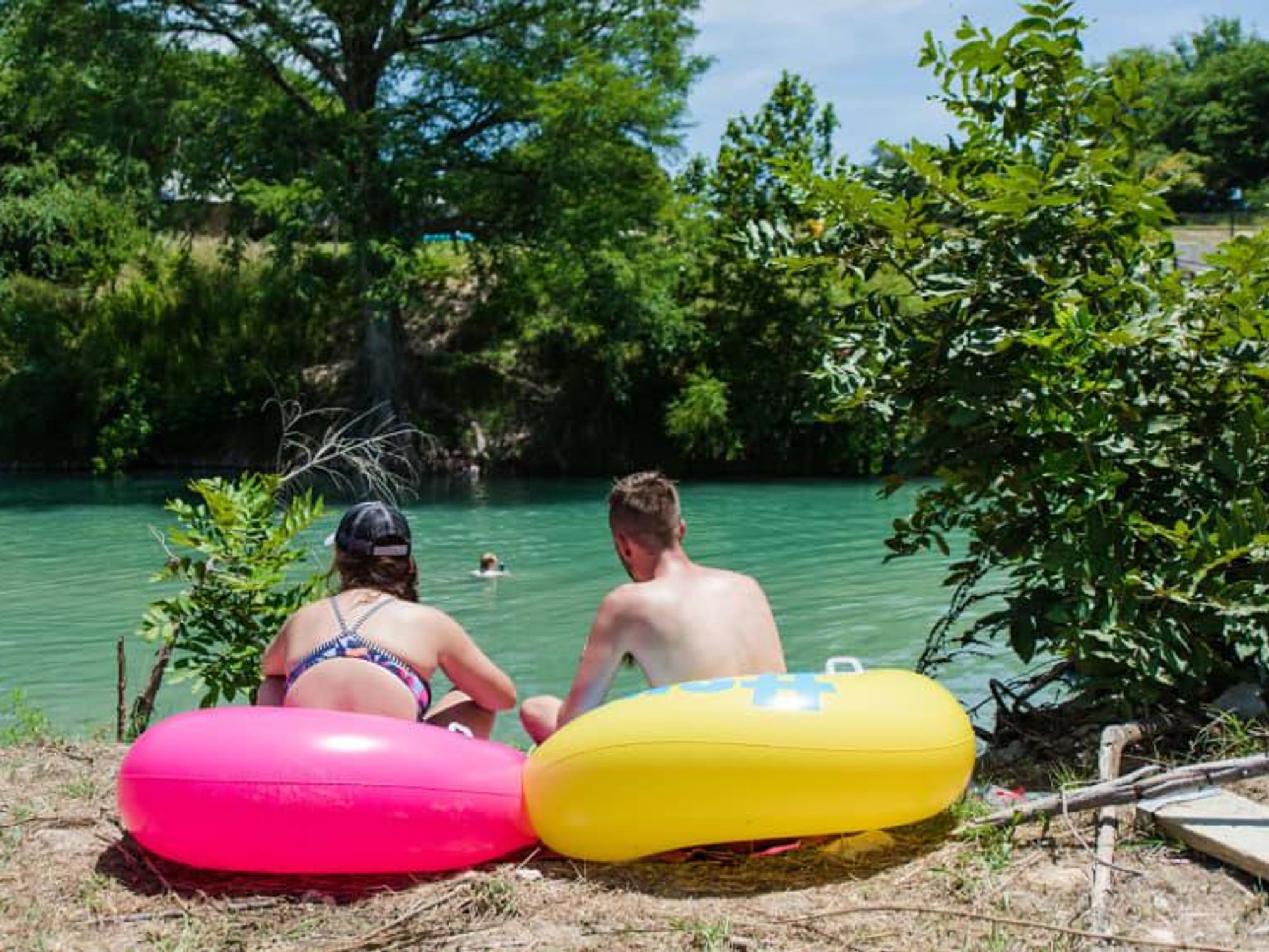 Two people sit in inner tubes facing the Guadalupe River during Float Fest.