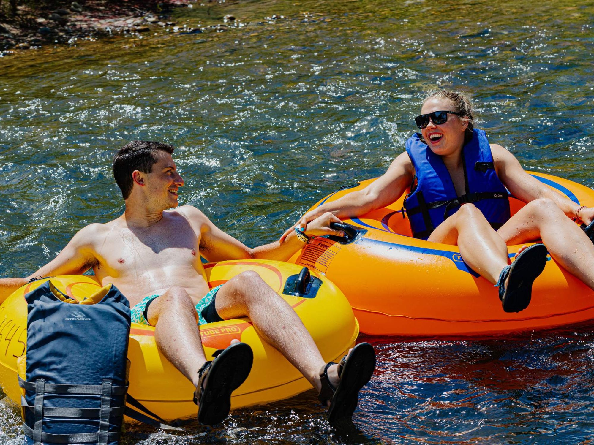 Two river tubers in orange and yellow river tubes, male and female , floating in the calm waters of Clear Creek holding hands