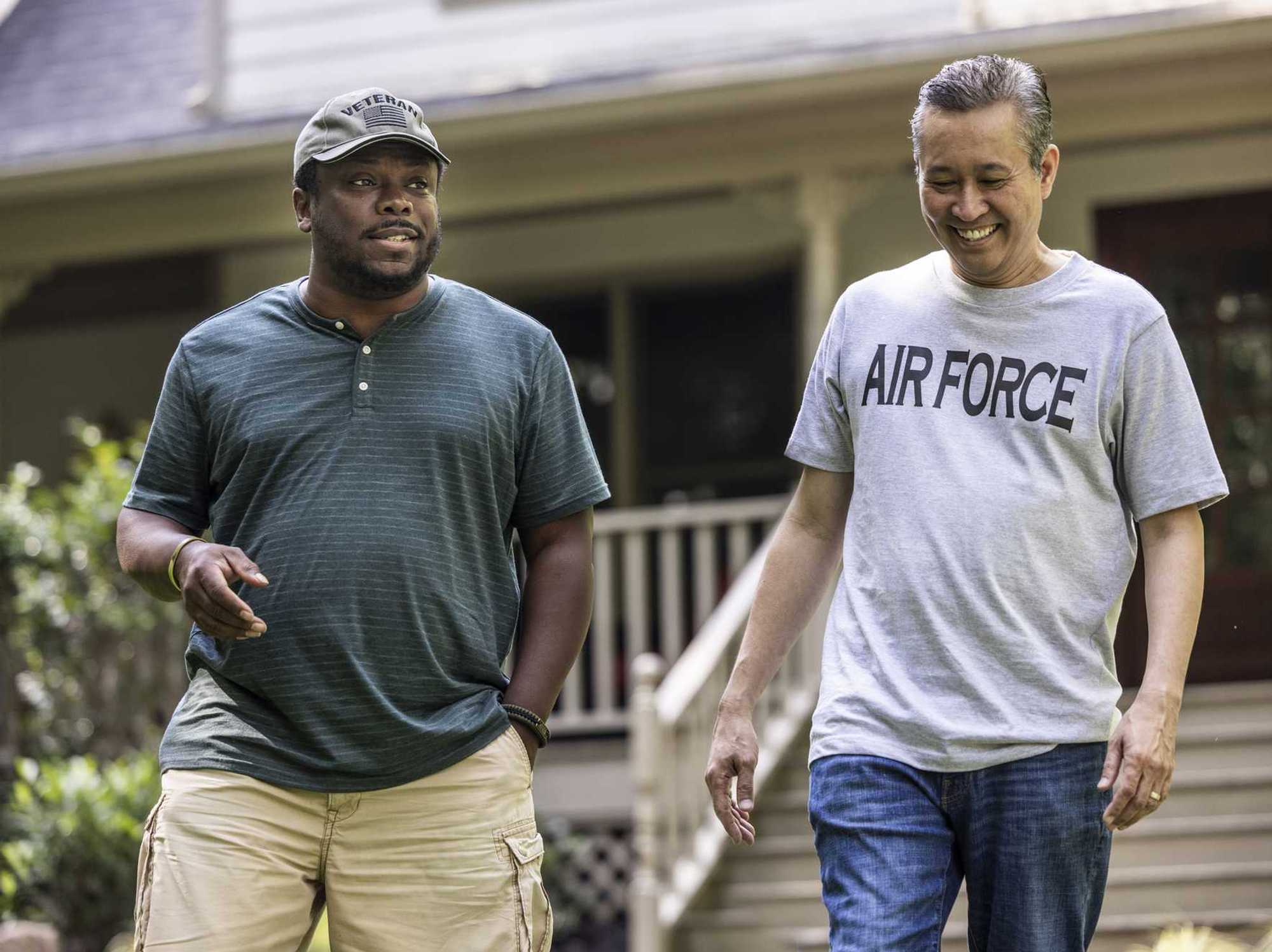 Two senior military veterans walking and talking in front of suburban home